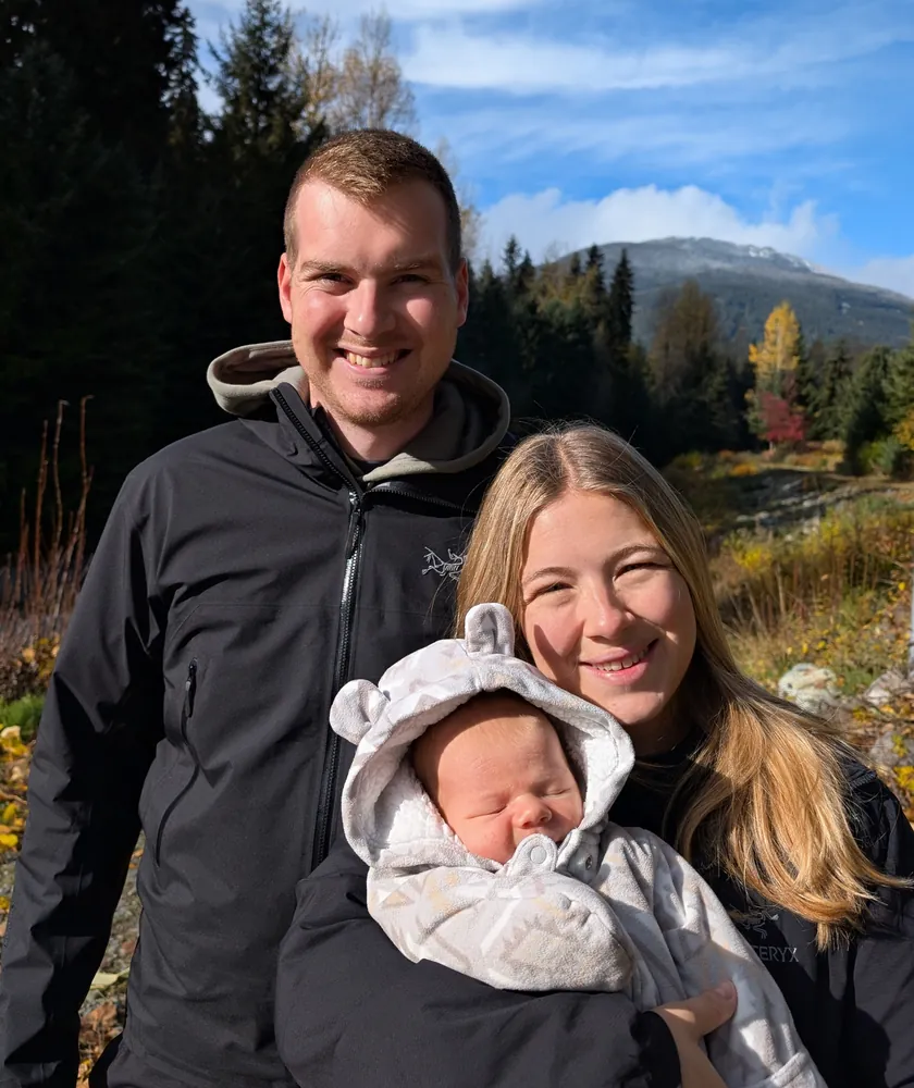 Andrew Flitton with his wife and their newborn, outdoors in the mountains in fall